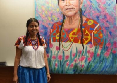 Foto de pintora Nahua Norma Martinez mostrando una pintura grande en La Universidad de Utah
