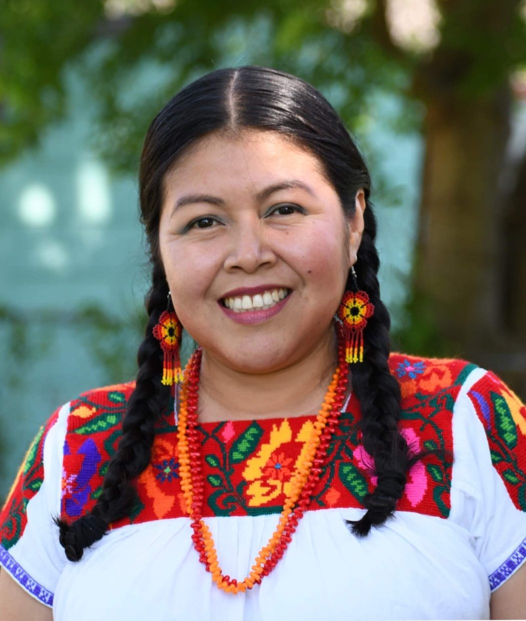 Foto de pintora Nahua, Norma Martinez, con blusa blanca bordada de colores rojos, amarillos, azules, vberdes y anaranjados. Nahua Art.